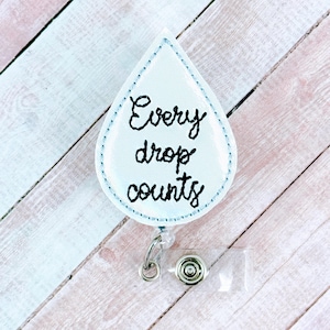 May include: White water drop shaped badge holder with the text "Every drop counts" embroidered in black thread.