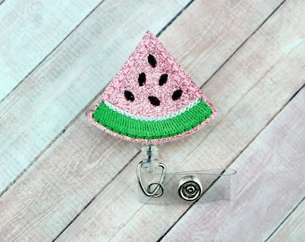 May include: Pink glitter watermelon slice badge reel with a green rind and black seeds. The reel is attached to a clear plastic badge holder with a metal clip.