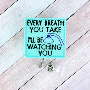 Puede incluir: Un portatarjetas turquesa con la frase bordada "EVERY BREATH YOU TAKE I'LL BE WATCHING YOU" en letras negras. También hay una ilustración azul de una lámpara. El portatarjetas tiene un clip plateado y una correa de plástico transparente.
