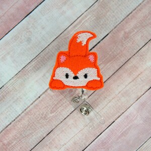 May include: Orange fox-shaped badge reel with a white face and a white tail. The reel is attached to a clear plastic badge holder.
