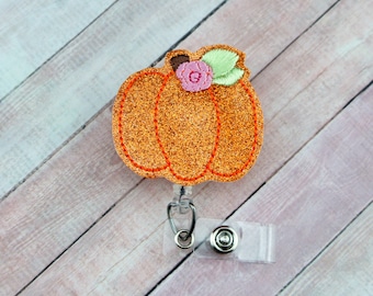 May include: Orange glitter pumpkin with a pink flower and green leaves on a retractable badge reel.