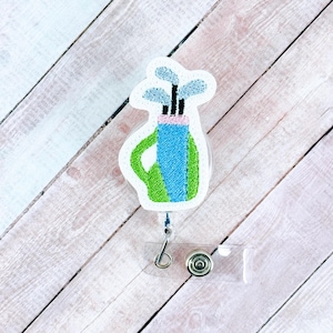 May include: A green and blue golf bag with golf clubs sticking out of the top. The bag is attached to a clear plastic retractable badge holder.