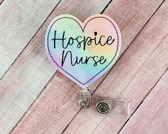 Könnte beinhalten: Ein regenbogenfarbener herzförmiger Badgehalter mit dem Text "Hospice Nurse" in schwarzen Buchstaben. Der Badgehalter ist an einer durchsichtigen, einziehbaren Badge-Rolle befestigt.