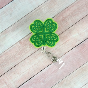 May include: Green shamrock-shaped badge reel with a Celtic knot design. The reel is attached to a clear plastic badge holder.