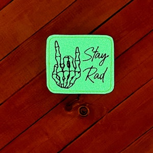 May include: Green square patch with a black skeleton hand giving the rock and roll sign. The text "Stay Rad" is written in black cursive.