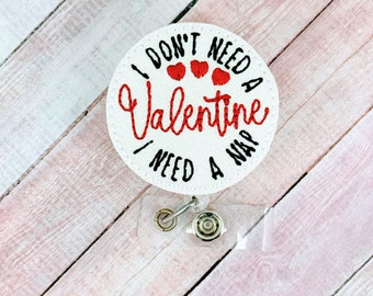 May include: White round badge holder with a black and red embroidered design that says "I don't need a Valentine I need a nap". Three red hearts are embroidered above the word "Valentine".