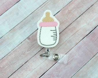 May include: White baby bottle with a pink and brown lid attached to a retractable badge reel. The reel is clear plastic with a silver clip.