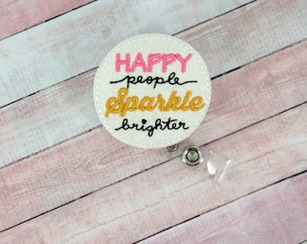 May include: White glitter badge reel with the text "Happy people sparkle brighter" in black, pink, and gold lettering.