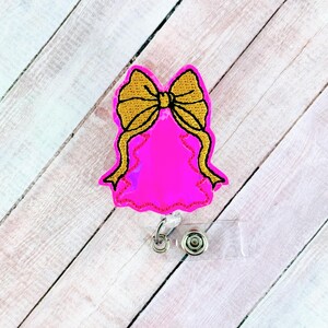 May include: A pink Christmas tree-shaped badge holder with a gold bow. The badge holder has a clear plastic retractable reel.