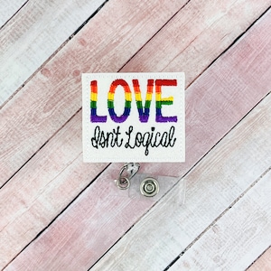 Könnte beinhalten: Ein weißes, quadratisches Ausweis-Jojo mit den Worten "LOVE Isn't Logical" in Regenbogenfarben und schwarzem Faden gestickt. Das Ausweis-Jojo hat einen transparenten Kunststoffhalter und einen silberfarbenen Metallclip.