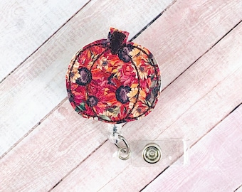 May include: A red, orange, and yellow floral patterned pumpkin-shaped badge holder with a clear plastic retractable badge reel.