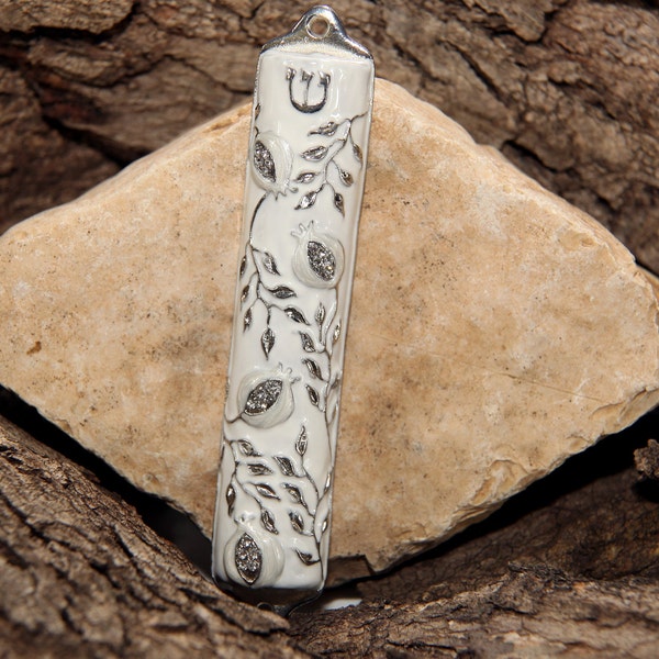 May include: White ceramic mezuzah with a silver design of pomegranates and leaves. The mezuzah has a silver Star of David at the top.