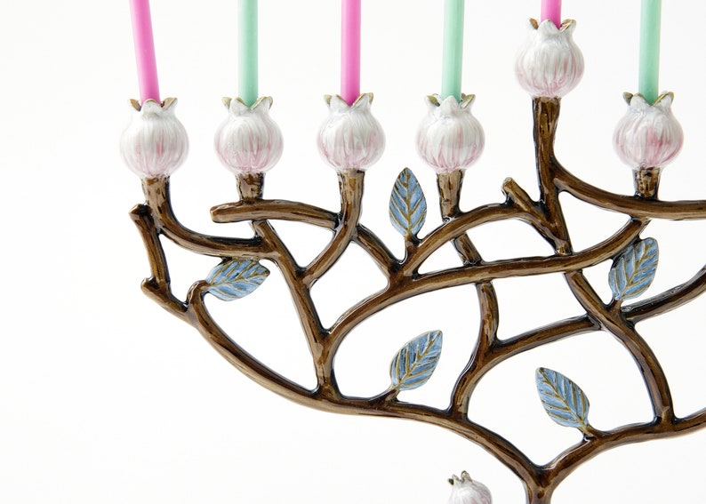 May include: A menorah with a tree branch design, featuring pink and blue floral accents. The menorah has eight candle holders and a shamash holder.