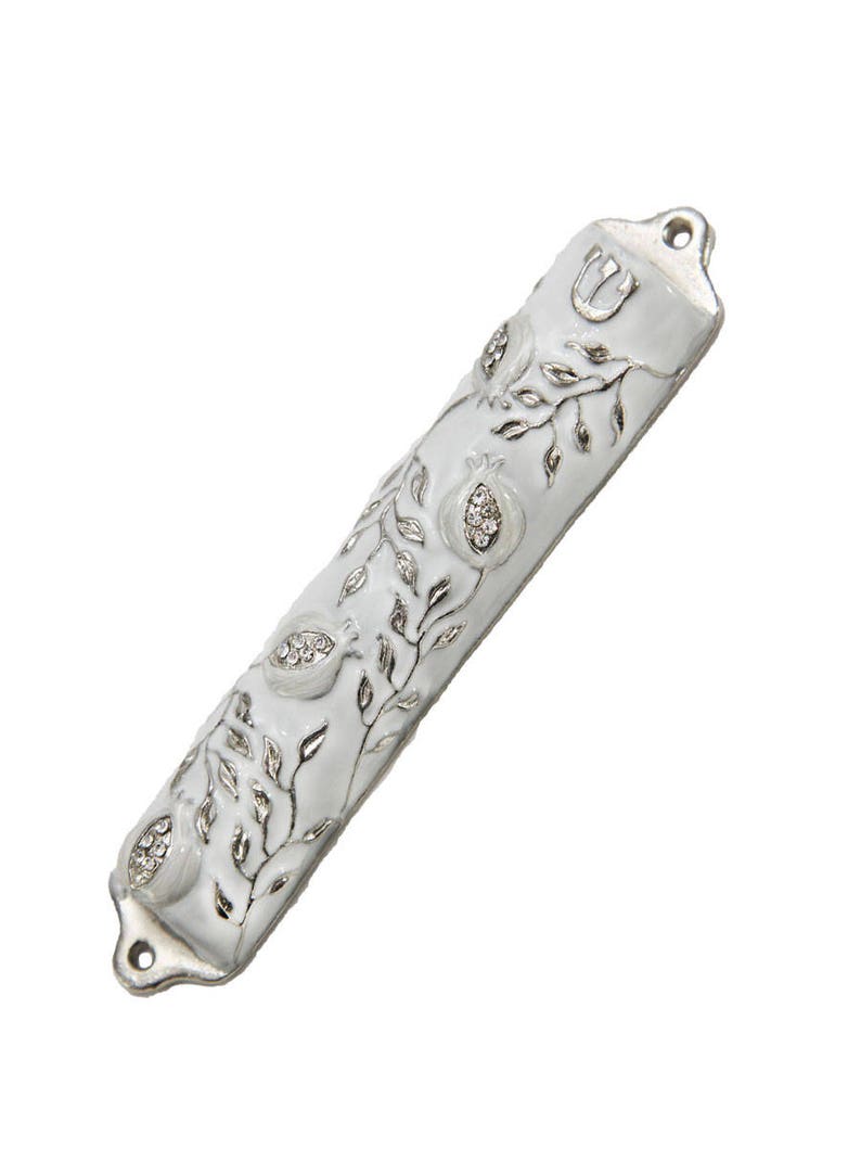 May include: White mezuzah with silver detailing of pomegranates and vines. The mezuzah has a silver Hebrew letter Shin on the top.