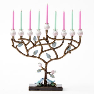 May include: A menorah shaped like a tree with pink and green candles. The menorah is decorated with blue birds and leaves. The base of the menorah is brown.