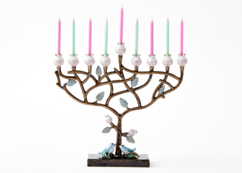 May include: A menorah shaped like a tree with pink and green candles. The menorah is decorated with blue birds and leaves. The base of the menorah is brown.