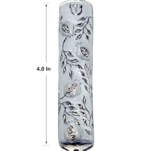 May include: White mezuzah with a silver design of pomegranates and leaves. The mezuzah is 10 cm tall and 2 cm wide.