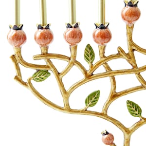 May include: Gold menorah with a tree branch design and orange and green enamel details. The menorah has nine candle holders and is decorated with leaves and fruit.