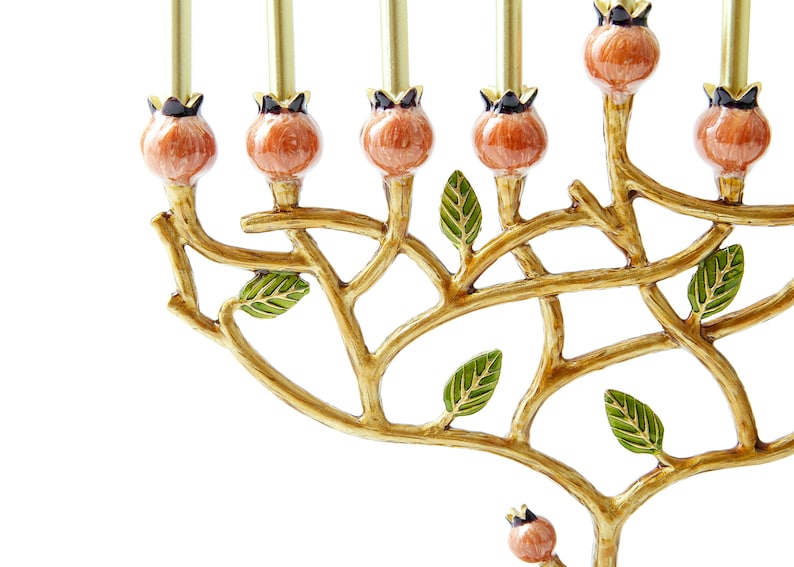 May include: Gold menorah with a tree branch design and orange and green enamel details. The menorah has nine candle holders and is decorated with leaves and fruit.