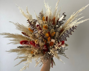 May include: A dried flower bouquet with a mix of pampas grass, dried eucalyptus, and red, orange, and white flowers.