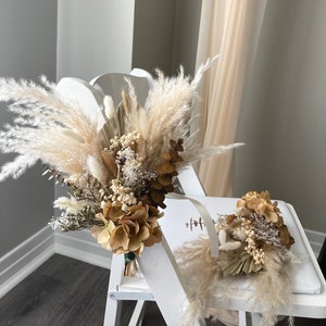Könnte beinhalten: Zwei Trockenblumensträuße im Boho-Stil mit Pampasgras, getrockneten Hortensien und anderen Trockenblumen. Die Sträuße sind auf einem weißen Stuhl arrangiert.