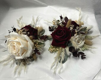 May include: Two floral arrangements with white and burgundy roses, dried grasses, and greenery.