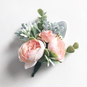 Puede incluir: Un pequeño ramo de flores de seda rosa claro con hojas verdes y detalles blancos. El ramo es perfecto para una boda u otra ocasión especial.