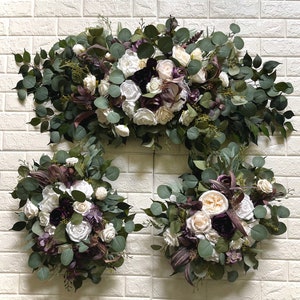 Può includere: Una ghirlanda per arco di matrimonio con fiori bianchi e bordeaux, verde e foglie di eucalipto. Due bouquet abbinati con fiori bianchi e bordeaux e verde.