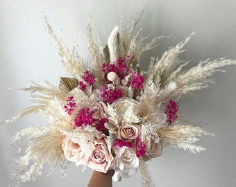 May include: A bouquet of dried flowers with pink and white roses, white pampas grass, and pink baby's breath.