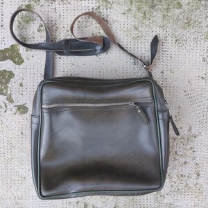 May include: A dark green leather messenger bag with a long adjustable strap and a zippered pocket on the front.