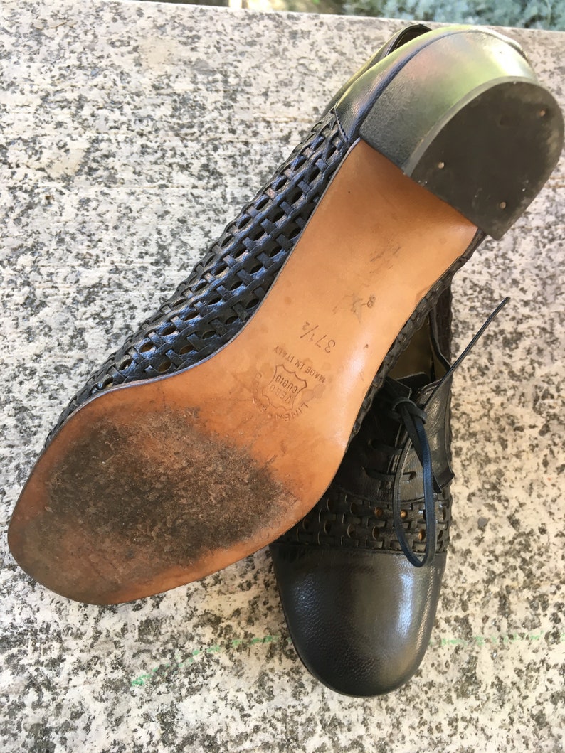Puede incluir: Zapatos de cuero negro con un dise&ntilde;o tejido y un tac&oacute;n bajo. Los zapatos est&aacute;n hechos en Italia y tienen una talla de 37 1/2.