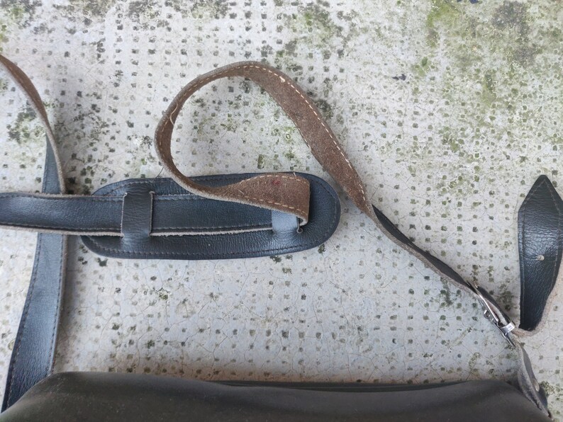 May include: A black leather camera strap with a brown leather adjustment strap. The strap has a metal buckle.