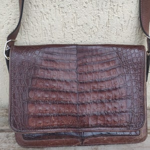 Peut inclure: Un sac à bandoulière en cuir marron avec un motif en relief de crocodile. Le sac a une fermeture à rabat et une longue bandoulière réglable.