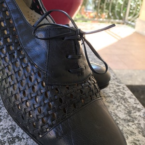 Puede incluir: Zapatos negros de cuero con cordones, con un patr&oacute;n tejido y punta cerrada.