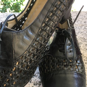 Puede incluir: Un par de zapatos de cuero negro con un dise&ntilde;o tejido y cierre de cordones. Los zapatos tienen un tac&oacute;n bajo y una punta puntiaguda.
