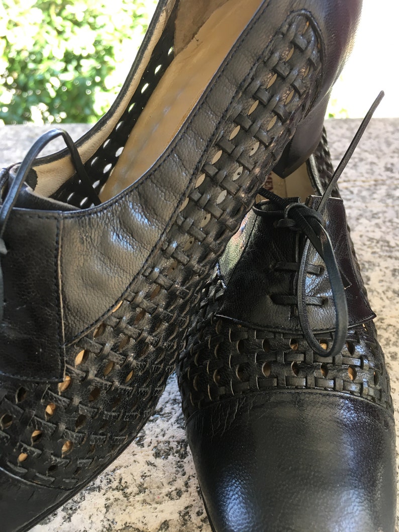 Puede incluir: Un par de zapatos de cuero negro con un dise&ntilde;o tejido y cierre de cordones. Los zapatos tienen un tac&oacute;n bajo y una punta puntiaguda.