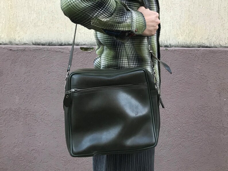 May include: A dark green leather messenger bag with a zippered pocket and a long adjustable strap.