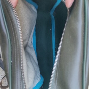 May include: A green leather bag with a zipper closure and a blue lining. The bag is open and the lining is visible.