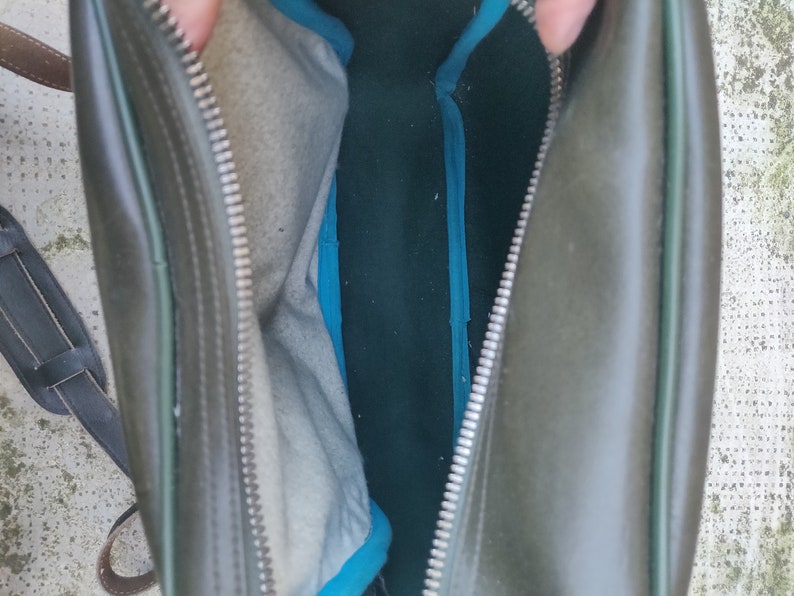 May include: A green leather bag with a zipper closure and a blue lining. The bag is open and the lining is visible.