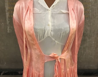 Op de afbeelding: Een roze satijnen badjas met een witte kantversiering en een strik in de taille.