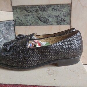 K&ouml;nnte beinhalten: Schwarze Leder-Tasssel-Slipper mit gewebtem Muster. Die Slipper haben eine spitze Zehenpartie und einen niedrigen Absatz.