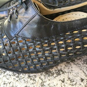 Puede incluir: Zapatos de cuero negro con un patr&oacute;n tejido y detalles recortados. Los zapatos tienen un tac&oacute;n bajo y cierre de cordones.