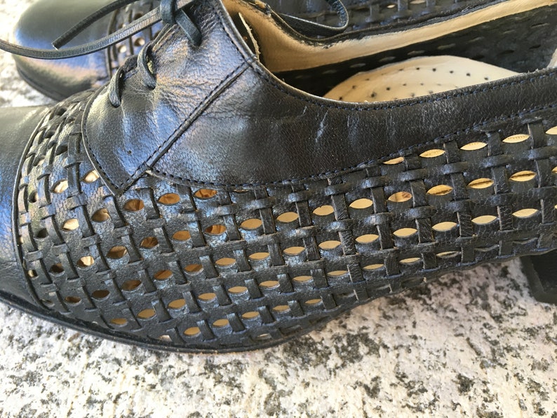 Puede incluir: Zapatos de cuero negro con un patr&oacute;n tejido y detalles recortados. Los zapatos tienen un tac&oacute;n bajo y cierre de cordones.
