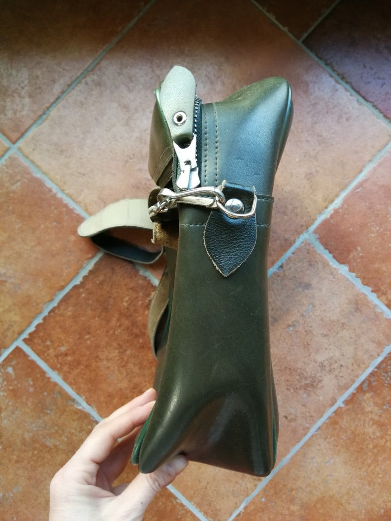 May include: A dark green leather satchel bag with a zipper closure and a strap. The bag has a silver buckle and a flap with a small leather tab.