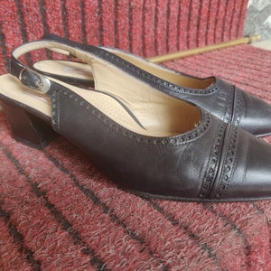 May include: A pair of black leather heeled slingback shoes with a decorative stitch pattern. The shoes have a closed toe and a slingback strap with a buckle.