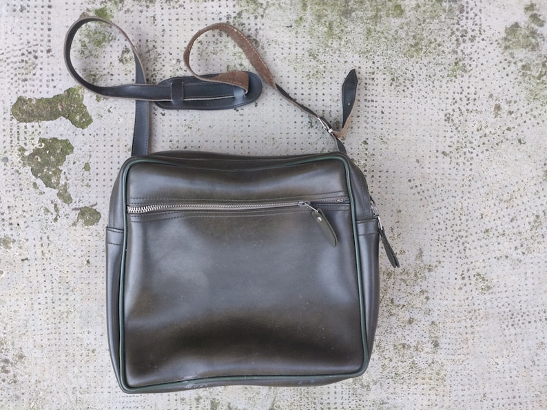 May include: A dark green leather messenger bag with a long adjustable strap and a zippered pocket on the front.