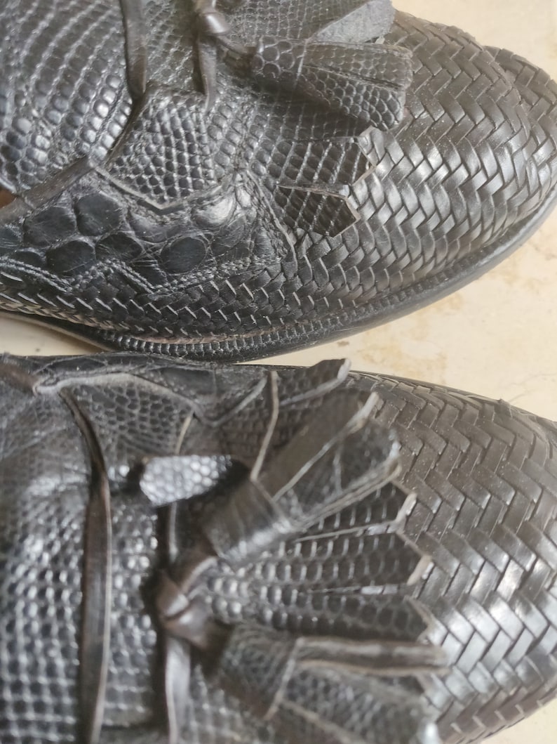 K&ouml;nnte beinhalten: Nahaufnahme eines Paares schwarzer Lederschuhe mit Quasten. Die Schuhe haben ein gewebtes Muster und eine strukturierte Oberfl&auml;che.