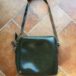 May include: A dark green leather shoulder bag with a long adjustable strap. The bag has a rectangular shape and a flap closure.