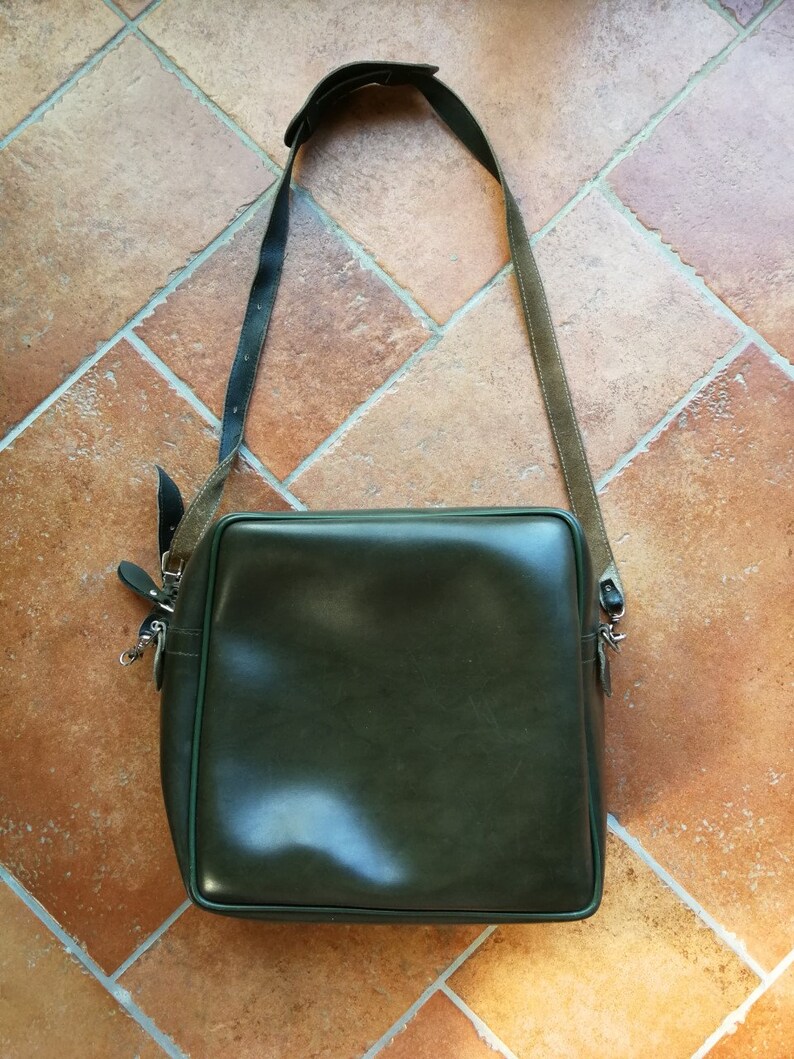 May include: A dark green leather shoulder bag with a long adjustable strap. The bag has a rectangular shape and a flap closure.