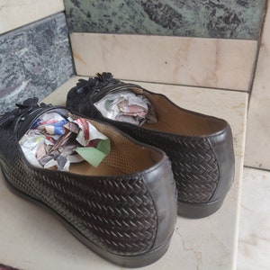 K&ouml;nnte beinhalten: Ein Paar braune Lederschuhe mit gewebtem Muster. Die Schuhe haben Quasten und sind mit zerknittertem Papier gef&uuml;llt.